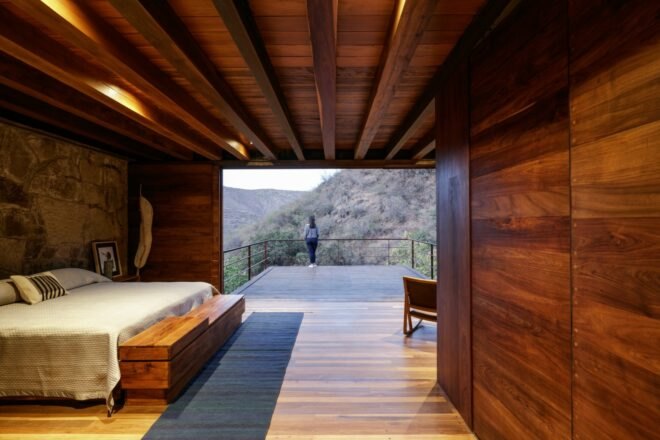 bedroom lined in wood and stone leading to outdoor terrace