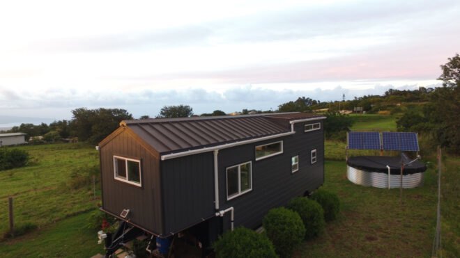 a tiny home clad in dark panels surrounded by greenery