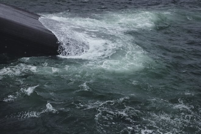 waves crashing against gray building jutting out from water