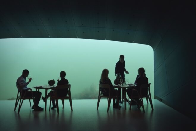 person serving food to people in room with glass wall revealing underwater views