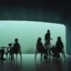 person serving food to people in room with glass wall revealing underwater views
