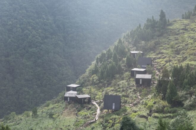 black wood cabins of different shapes and sizes on a green mountain