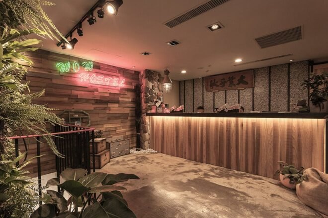 wooden reception desk and wood wall with neon sign that reads Wow Hostel
