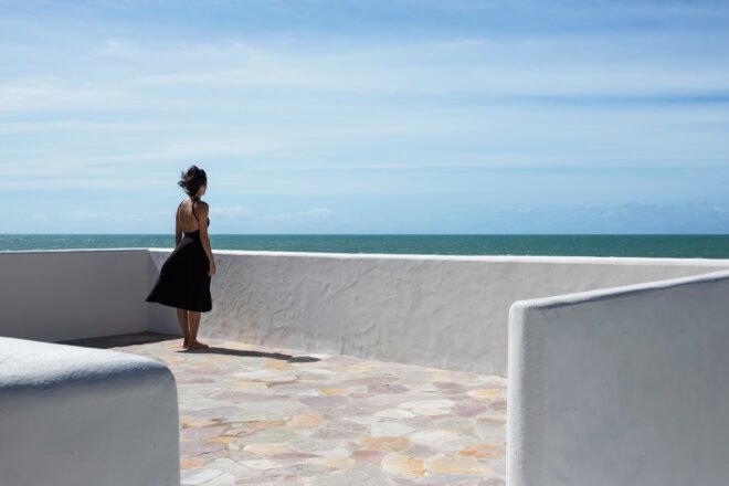 woman stands on home's roof during a sunny day looking out onto the ocean