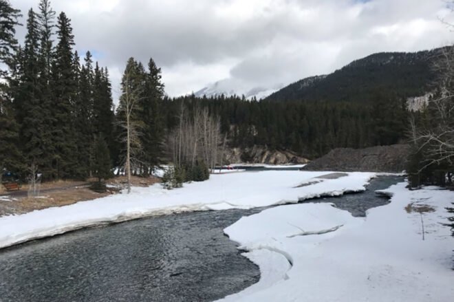 snow surrounds an icy lake surrounded by greenery near the hotel