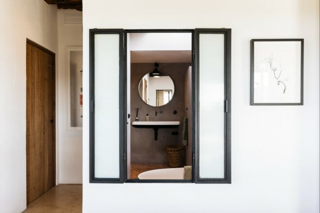 interior window in a bedroom open to reveal a gray bathroom