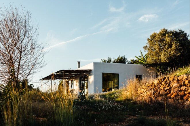 White, cube-like structure with front porch surrounded by plants