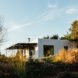 White, cube-like structure with front porch surrounded by plants