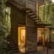 wood treehouse with wood spiraled stairs surrounded by forest with interior lights illuminating the home