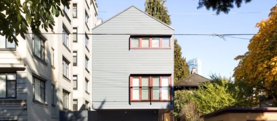 narrow gray building with red framed windows and a gabled roof