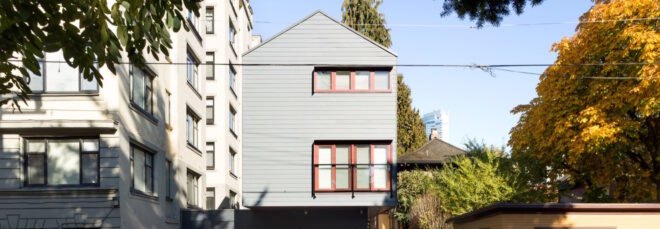 narrow gray building with red framed windows and a gabled roof