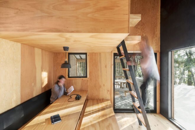 one person sitting at table reading a book and another person climbing ladder up to a loft