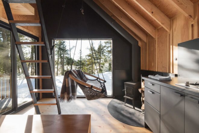 suspended chair near a fireplace and large window with views of snowy forestscape