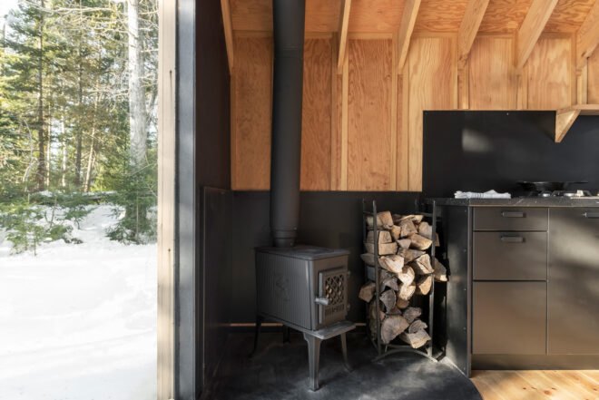 black wood-burning stove with stack of firewood next to it