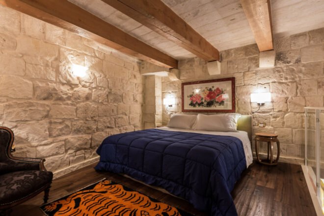 guest room with large bed, stone walls and wood ceiling beams