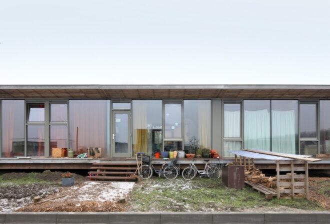 long wood building raised from the ground in a large open land with grass and snow