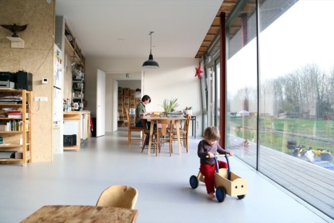interior of home with white walls and large windows illuminating the dining area as a child plays near the window in a wood car