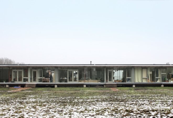 long wood building raised from the ground in a large open land with grass and snow
