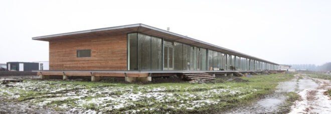 long wood building raised from the ground in a large open land with grass and snow