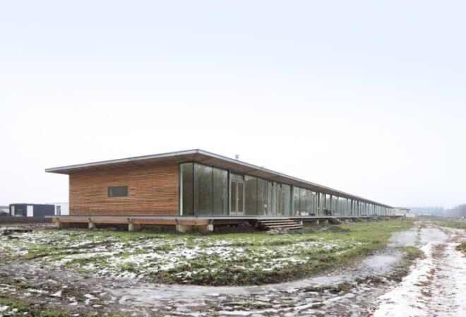 long wood building raised from the ground in a large open land with grass and snow