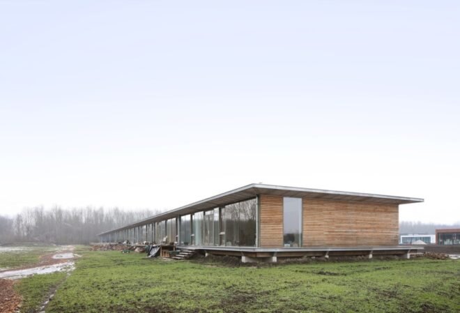 long wood building raised from the ground in a large open land with grass and snow