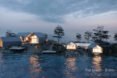 rendering of gabled wood and glass cabins on a island at dusk