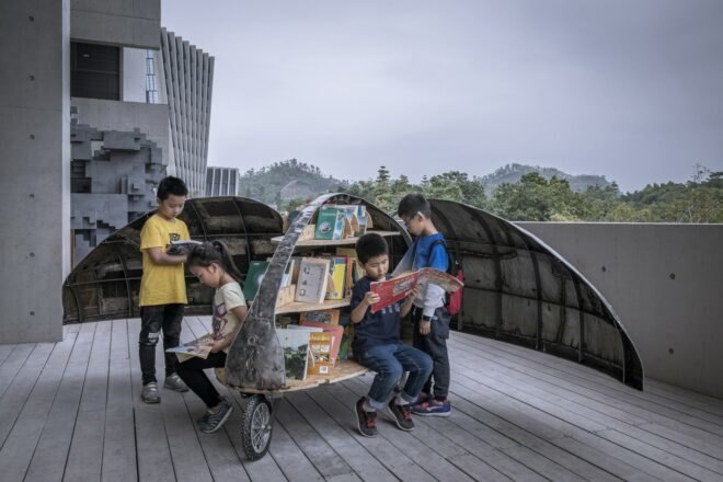 children checking out books from a metal contraption on wheels in the shape of a beetle