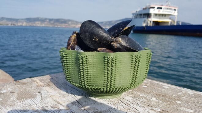 seafood in a green 3D-printed bowl perched on wood table by the sea
