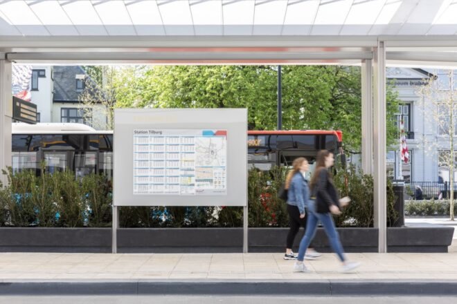 people walking past board with bus schedules