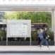 people walking past board with bus schedules