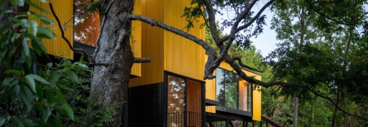 elevated vibrant yellow prefab home surrounded by greenery