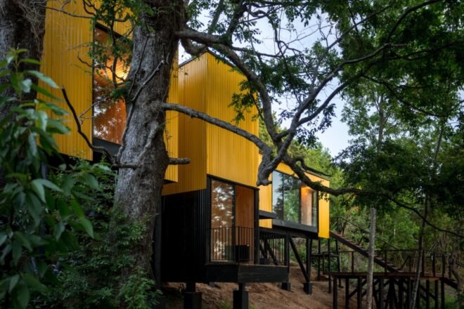 elevated vibrant yellow prefab home surrounded by greenery