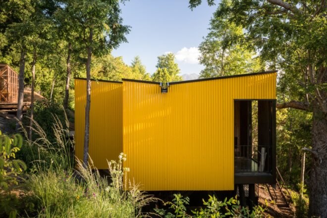 elevated vibrant yellow prefab home surrounded by greenery