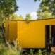 elevated vibrant yellow prefab home surrounded by greenery