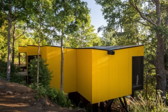 elevated vibrant yellow prefab home surrounded by greenery