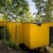 elevated vibrant yellow prefab home surrounded by greenery