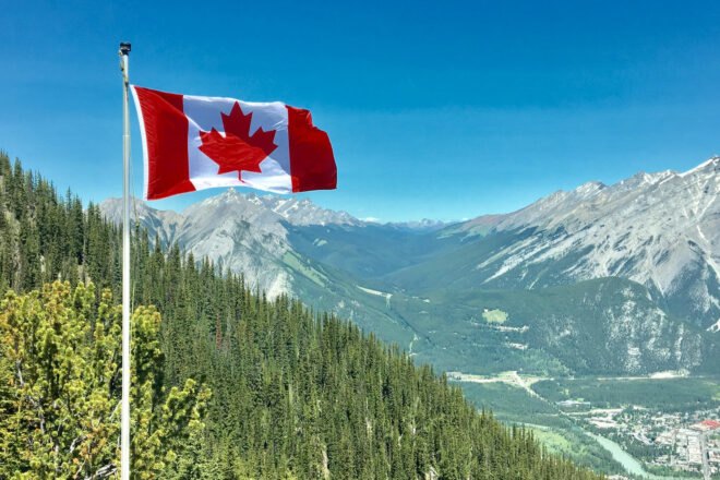 Canadian flag with green forest and mountains in background