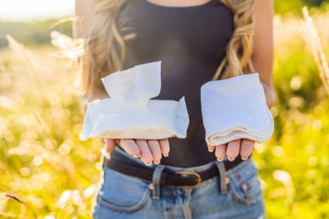 woman holding package of wipes in one hand and reusable cloth in another