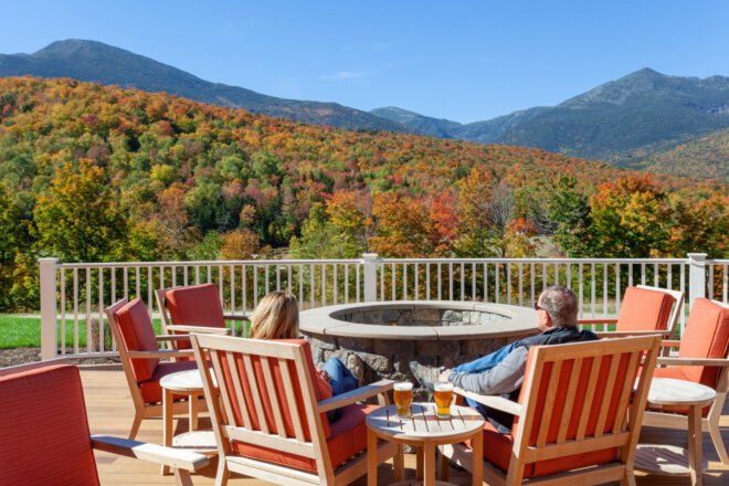 Guests sit by a firepit and look at the fall colors on the mountains.
