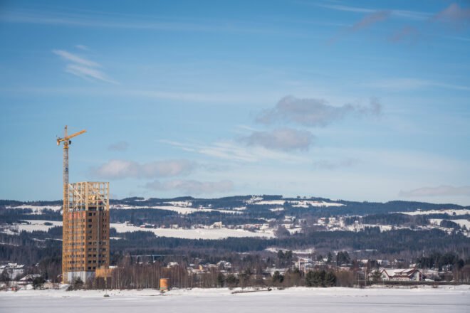 tall wood building under construction with snow-capped mountains in distance