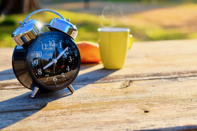 black alarm clock sits on wooden table next to yellow coffee cup
