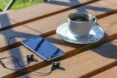 smartphone and earbuds next to cup of coffee on wood table