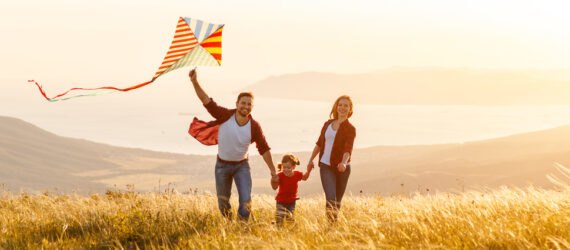 a family runs through a grassy field with a kite