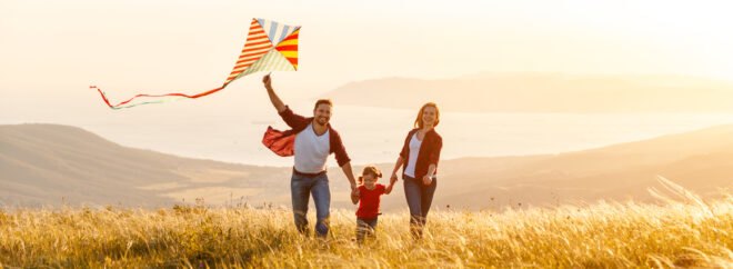 a family runs through a grassy field with a kite