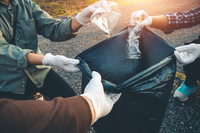 people throwing plastic bottles into a black bag