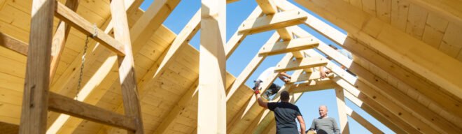 two men build a roof on a house