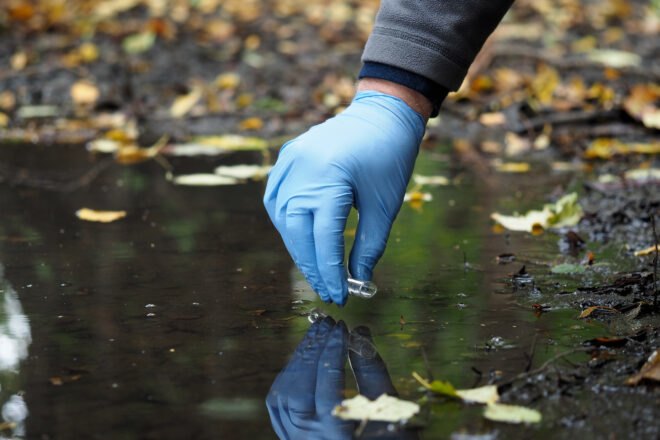person wearing blue glove with a test tube collects water sample