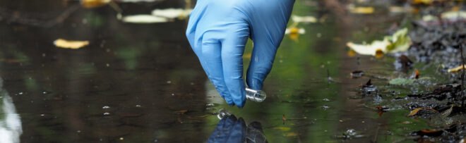 person wearing blue glove with a test tube collects water sample