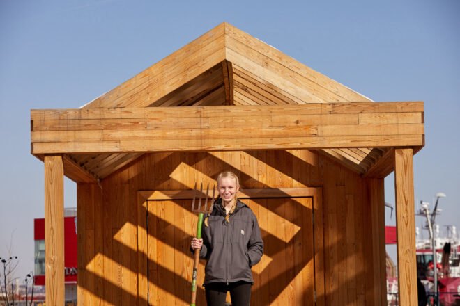 woman with pitchfork in front of wood garden shed