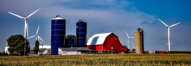 wind turbines beside red barns and silos
